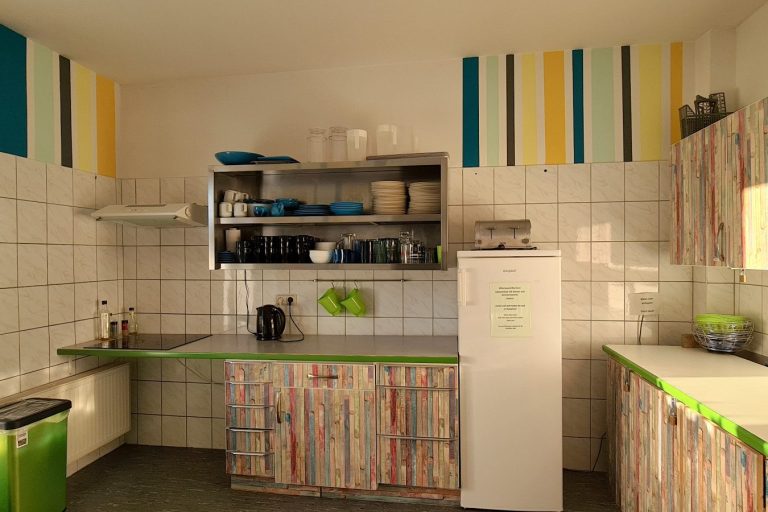 Gästeküche Helle Küche mit bunten Wänden, Geschirr im Regal und einer modernen Kühl-/Gefrierkombination.