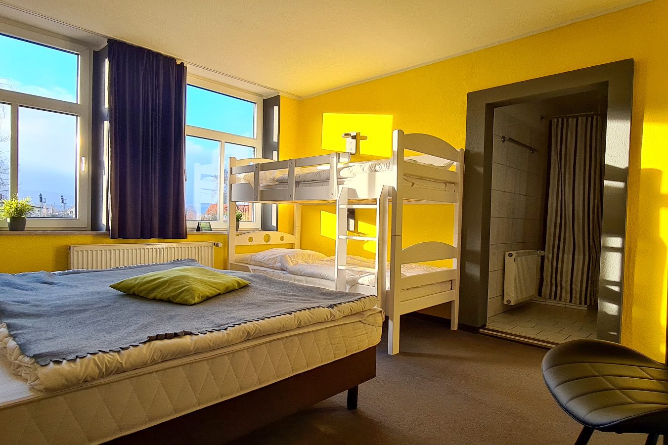Familienzimmer für 4 Personen Helles Zimmer mit einem Doppelbett, Etagenbett und einem Bad im Hintergrund.