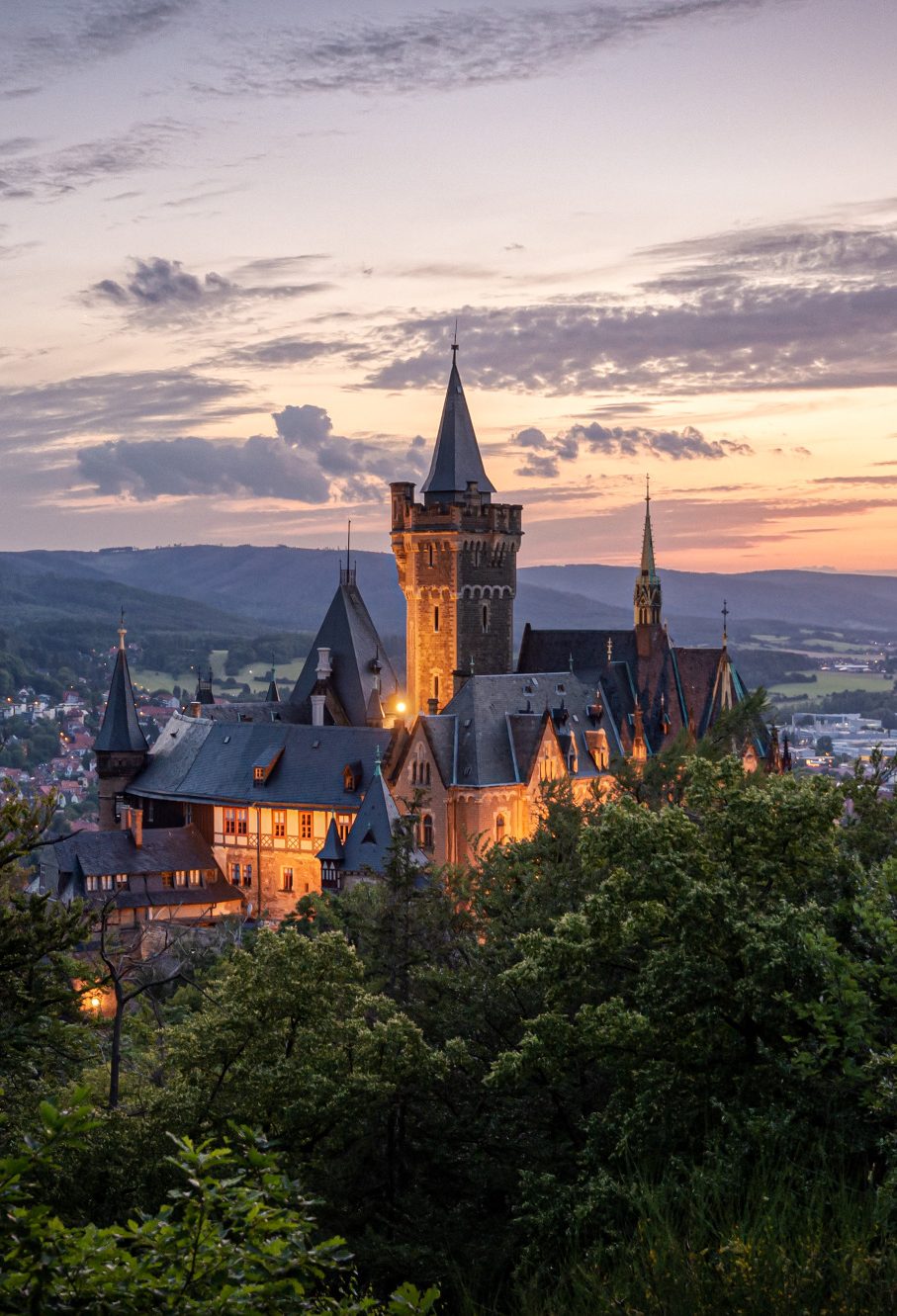 Wernigeröder Schloss Blick auf eine beleuchtete Burg bei Sonnenuntergang, umgeben von Hügeln.