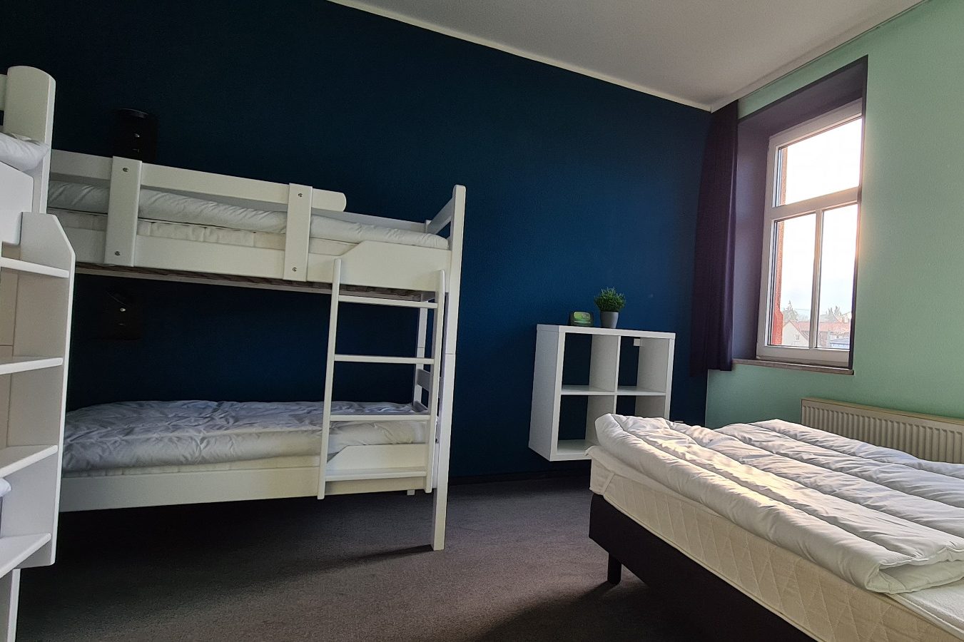 Mehrbettzimmer Ein Zimmer mit einem Etagenbett, einem Einzelbett und einem Regal.